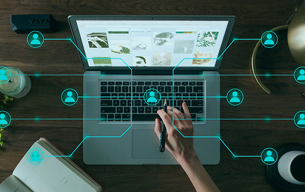 The image shows a computer on a work desk, symbolizing a tool used to communicate with the rest of the world. In the foreground of the image, a graph is illustrated, consisting of nodes shaped like silhouettes of people and edges connecting them. This represents interconnectivity and highlights the importance of technological tools for interacting with the global community.